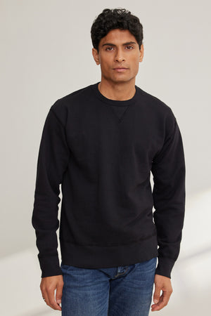 A man with short black hair wears the RAE SWEATSHIRT by Velvet by Graham & Spencer and blue jeans, standing facing the camera against a neutral background.