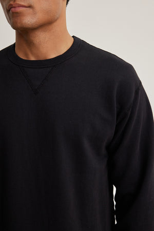 A person wearing the RAE SWEATSHIRT by Velvet by Graham & Spencer, a plain black French terry crew neck, is shown from shoulders to mid-torso, facing forward.