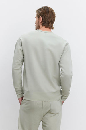 A man with light brown hair is wearing a Velvet by Graham & Spencer RAE SWEATSHIRT and matching pants, standing with his back facing the camera against a plain white background.