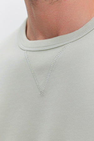 Close-up of a person wearing a light grey Velvet by Graham & Spencer RAE SWEATSHIRT, showcasing the stitching details near the neckline.
