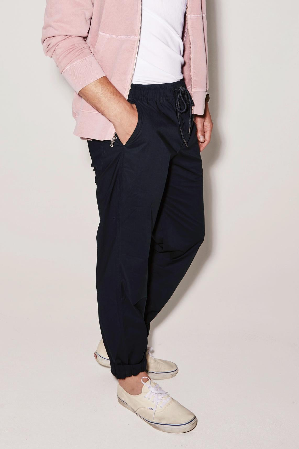 Man standing in a relaxed pose, wearing a pink jacket, white shirt, Velvet by Graham & Spencer Lazarus Jogger trousers, and light-colored shoes. Only the lower half of his body is visible.-36732528820417