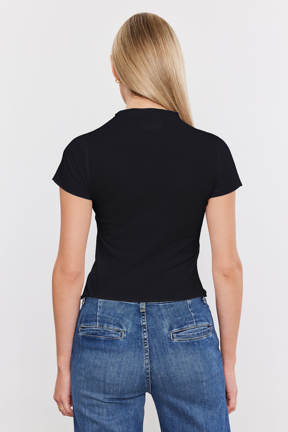 Woman viewed from behind wearing a black Velvet by Graham & Spencer JACKIE MOCK NECK TEE and blue jeans, standing against a white background.-36909390627009