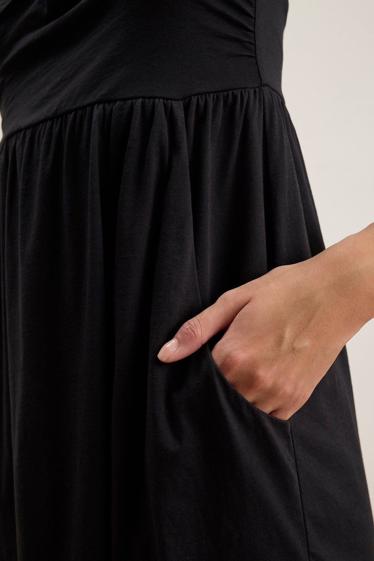 A person slips their right hand into the side pocket of the BARBI DRESS by Velvet by Graham & Spencer, a black mini dress ideal for warm days.-39145472360641