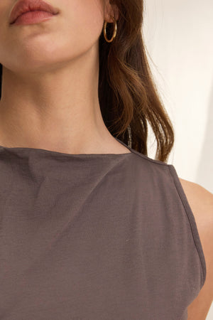 Close-up of a person wearing the EMILIA TANK TOP by Velvet by Graham & Spencer, a gauzy whisper of gray with a gold hoop earring and long brown hair partially visible.