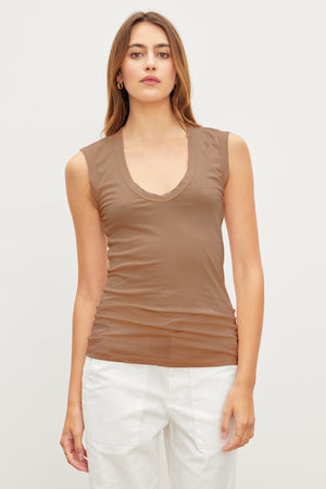 A long-haired person wears a brown ESTINA TANK TOP by Velvet by Graham & Spencer and white pants, standing against a plain light background.