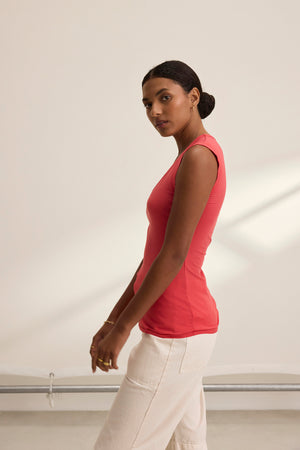 Wearing a Velvet by Graham & Spencer ESTINA TANK TOP and beige pants, a person stands sideways against a neutral backdrop.