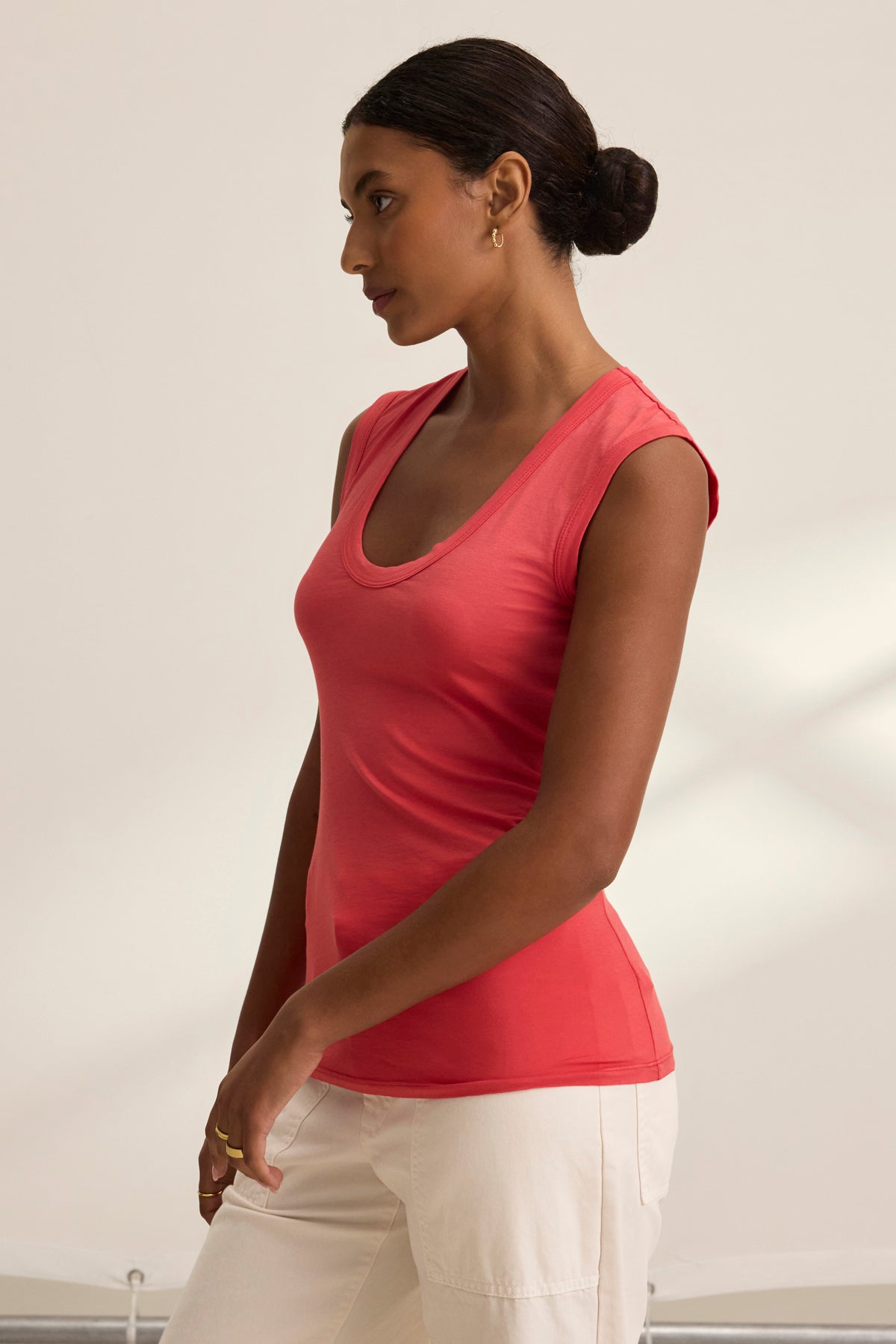 A person in a whisper pink ESTINA TANK TOP by Velvet by Graham & Spencer and white pants stands sideways, facing left with hair in a bun against a plain background.-38928283304129