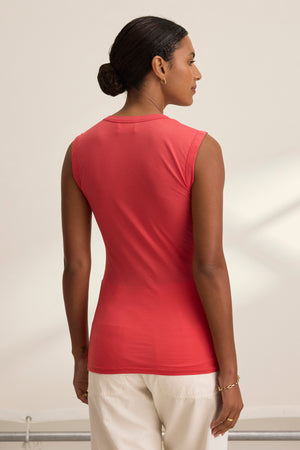 A person facing away is wearing the ESTINA TANK TOP in red by Velvet by Graham & Spencer, paired with white pants. Hair is styled in a bun.