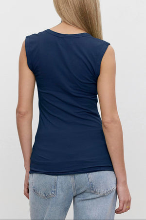 A person with long, straight hair in a Velvet by Graham & Spencer ESTINA TANK TOP and light blue jeans is standing and facing away from the camera.