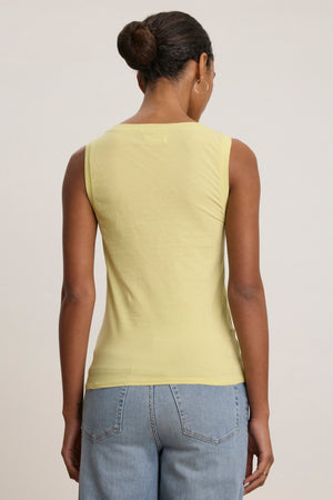 A person with their hair in a bun models the EVELYN TANK TOP by Velvet by Graham & Spencer in yellow, paired with light blue jeans, shown from the back against a plain light background.