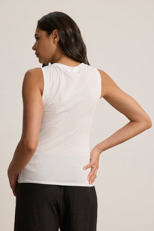 A person with long dark hair wears the EVELYN TANK TOP by Velvet by Graham & Spencer and black pants, standing with their back to the camera, one hand on their hip, showcasing this timeless wardrobe essential.
