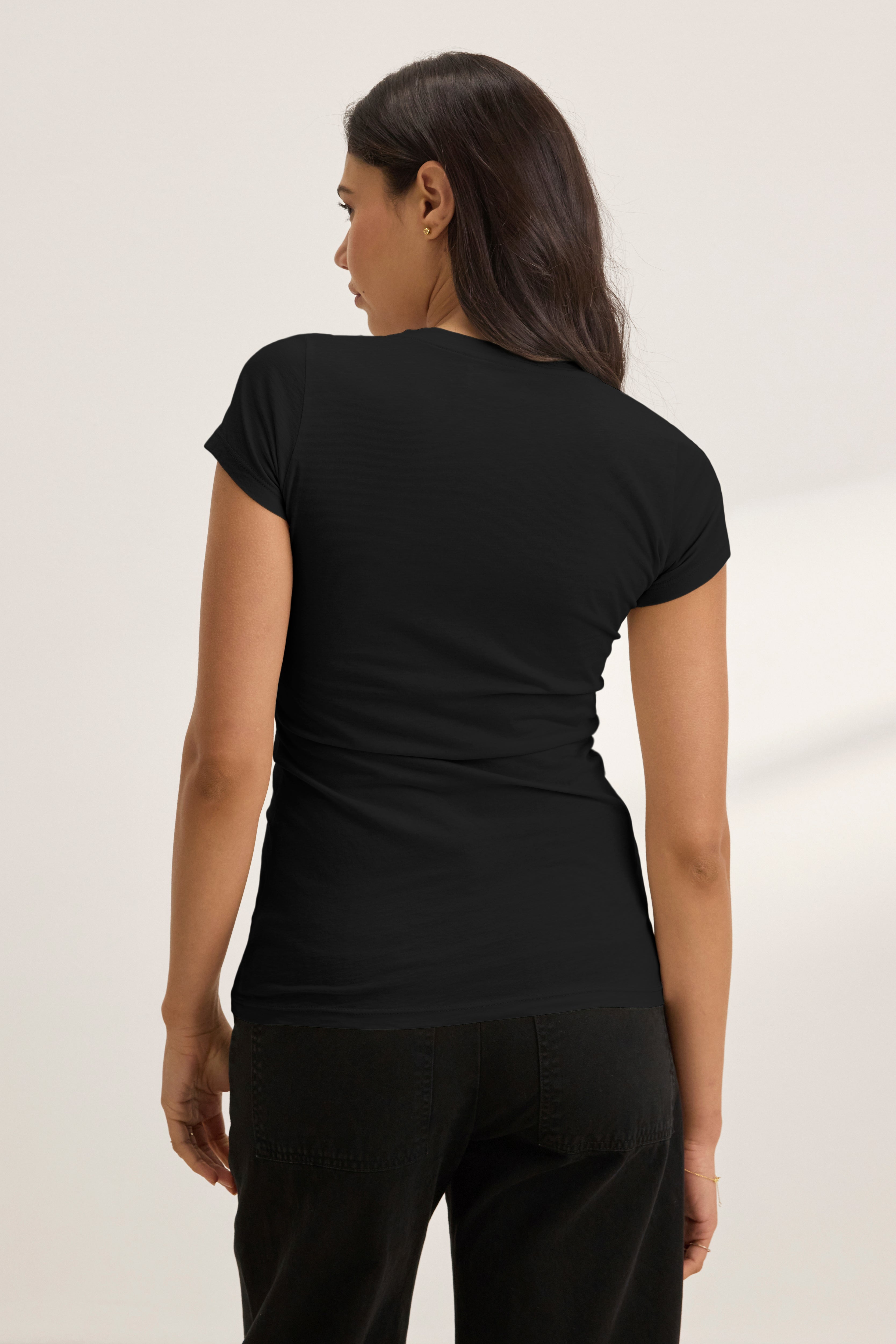 A woman with long dark hair stands facing away, wearing the JEMMA TEE by Velvet by Graham & Spencer in black with matching black pants, set against a neutral background.
