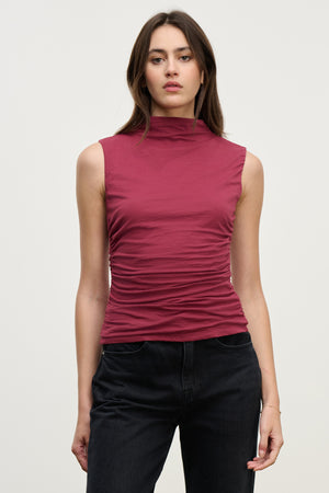 A woman stands facing the camera against a plain light background, wearing the Velvet by Graham & Spencer MADELINE TANK TOP in maroon gauzy whisper fabric paired with black jeans.