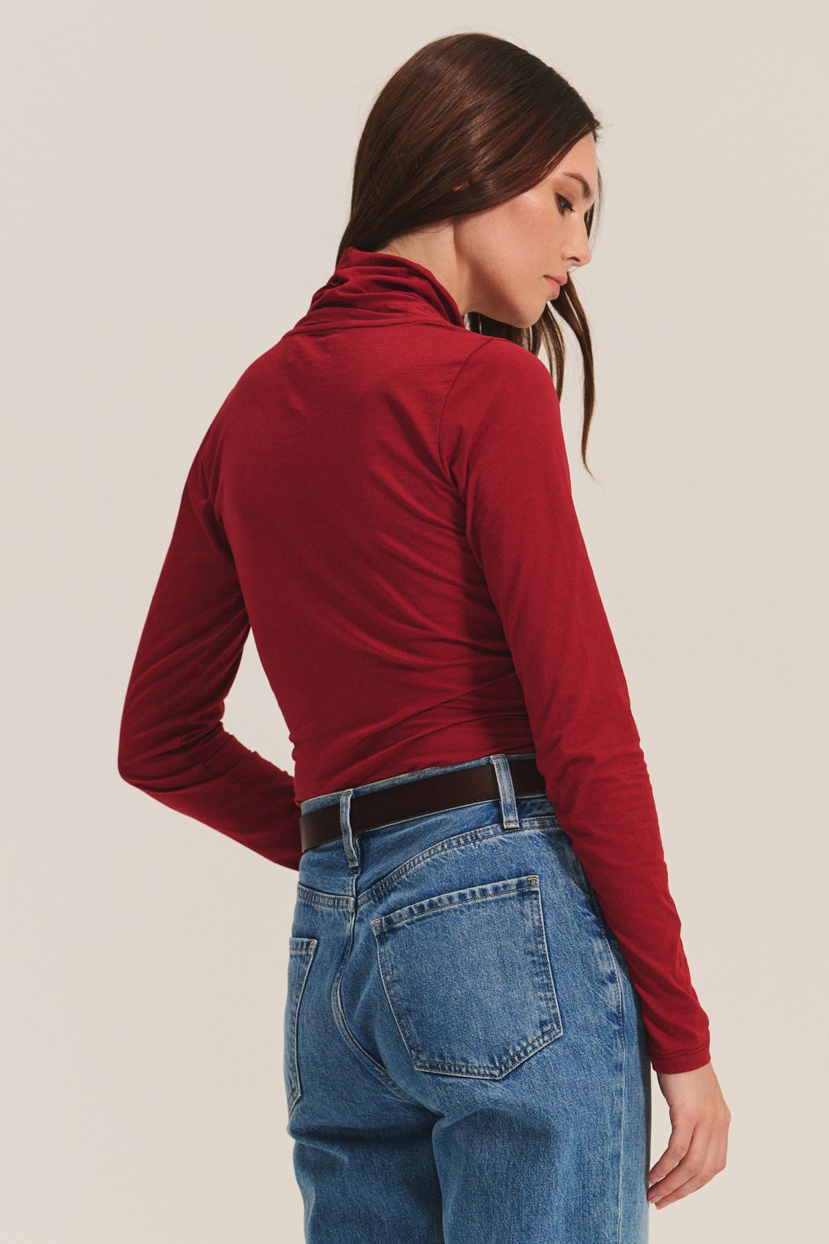 A woman wearing the MERI TEE by Velvet by Graham & Spencer and blue jeans stands facing away with one hand in her pocket against a plain background.-40182501376193