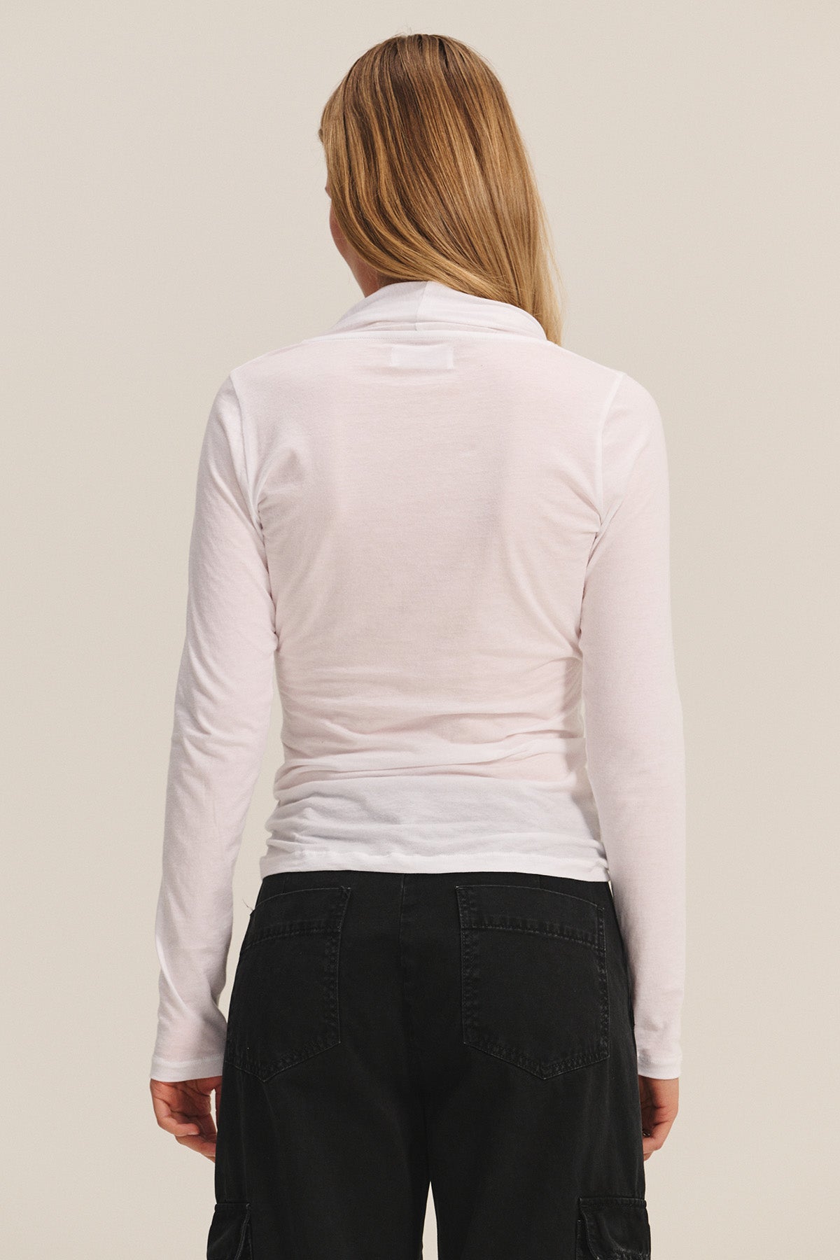 A person with long blonde hair is shown from the back, wearing the MERI TEE by Velvet by Graham & Spencer—a light pink fitted V-neck t-shirt—and black pants against a plain background.