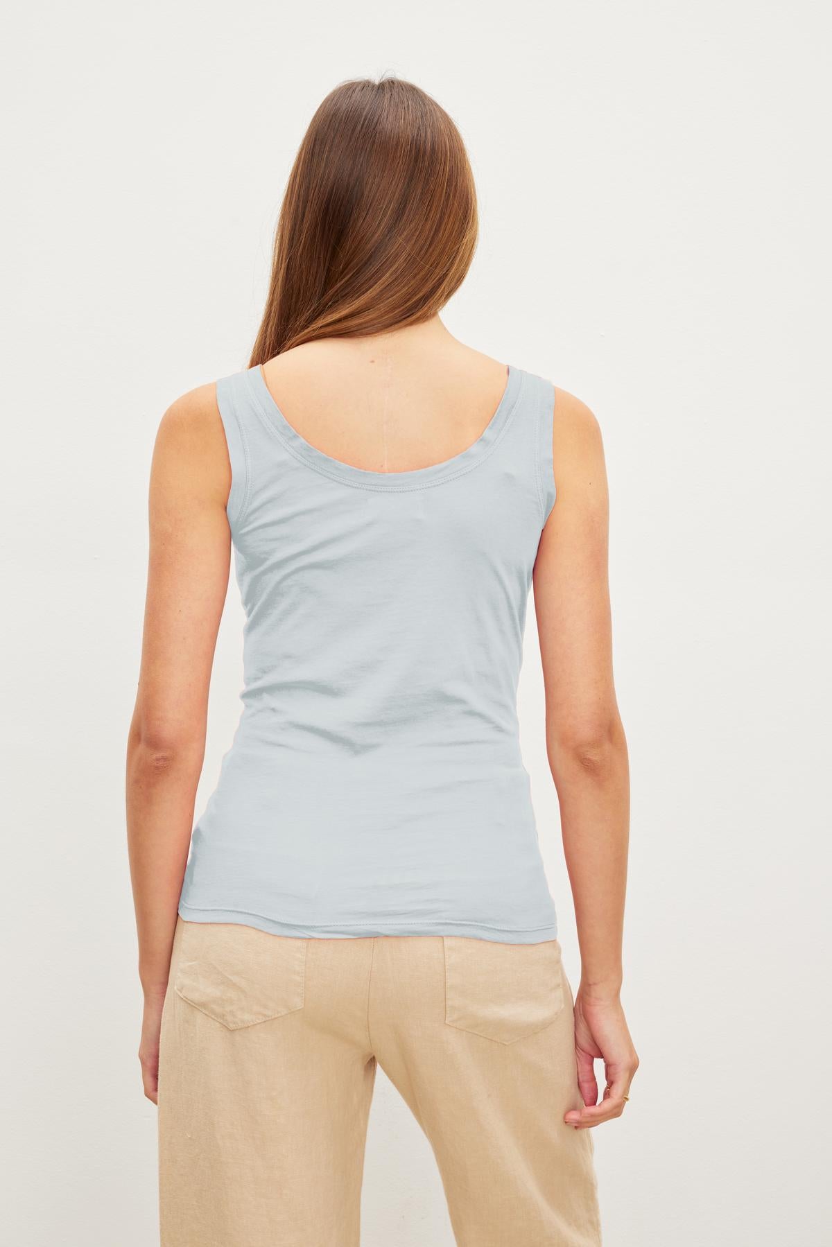 Woman with long brown hair wearing a Velvet by Graham & Spencer MOSSY TANK TOP and beige pants, facing away from the camera, epitomizes effortless style and versatility.-37241163251905