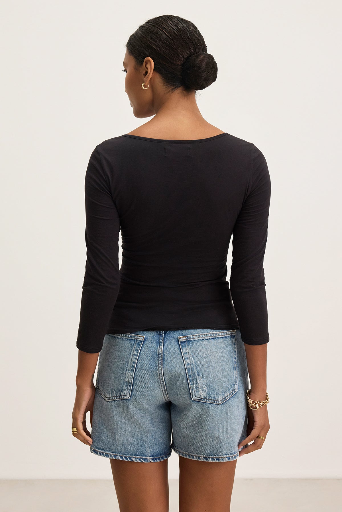 A person wearing the SETT TEE from Velvet by Graham & Spencer is shown from the back, paired with denim shorts. The black, gauzy whisper fabric top with 3/4 sleeves complements the casual look against a plain background.