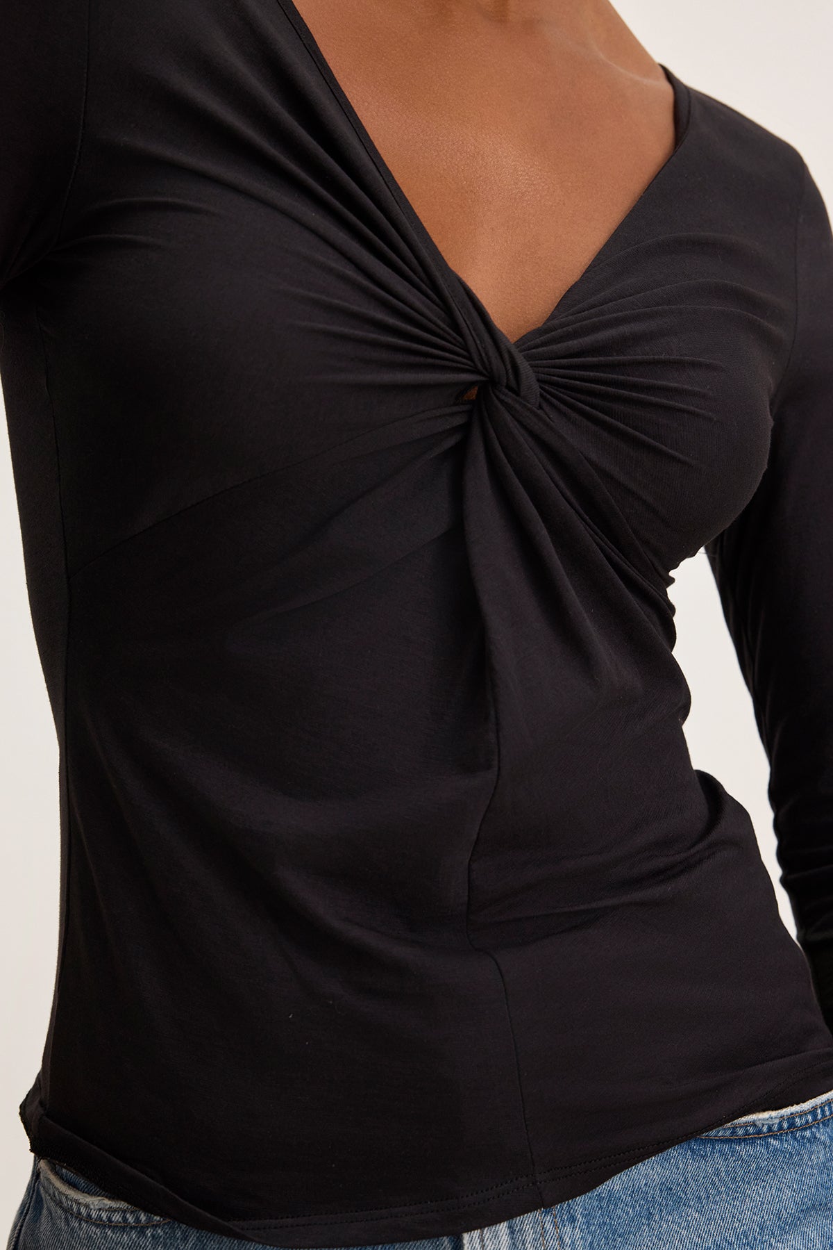 A person is wearing the SETT TEE, a black long-sleeve top with a twist knot front, by Velvet by Graham & Spencer, crafted from gauzy whisper fabric, paired gracefully with blue jeans.-38663161249985