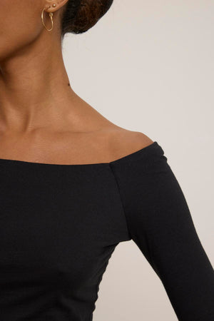 Someone wearing the TANYA TEE by Velvet by Graham & Spencer paired with hoop earrings, photographed from the neck down against a plain background.