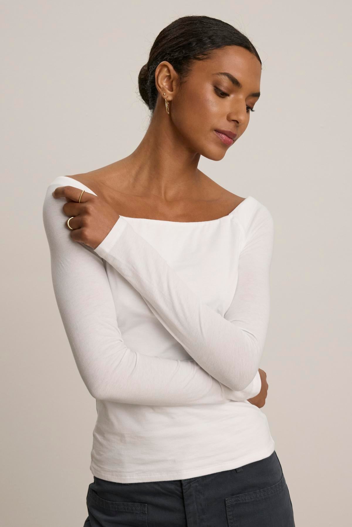 A person poses with their arms crossed, wearing the TANYA TEE by Velvet by Graham & Spencer and dark pants against a neutral background.