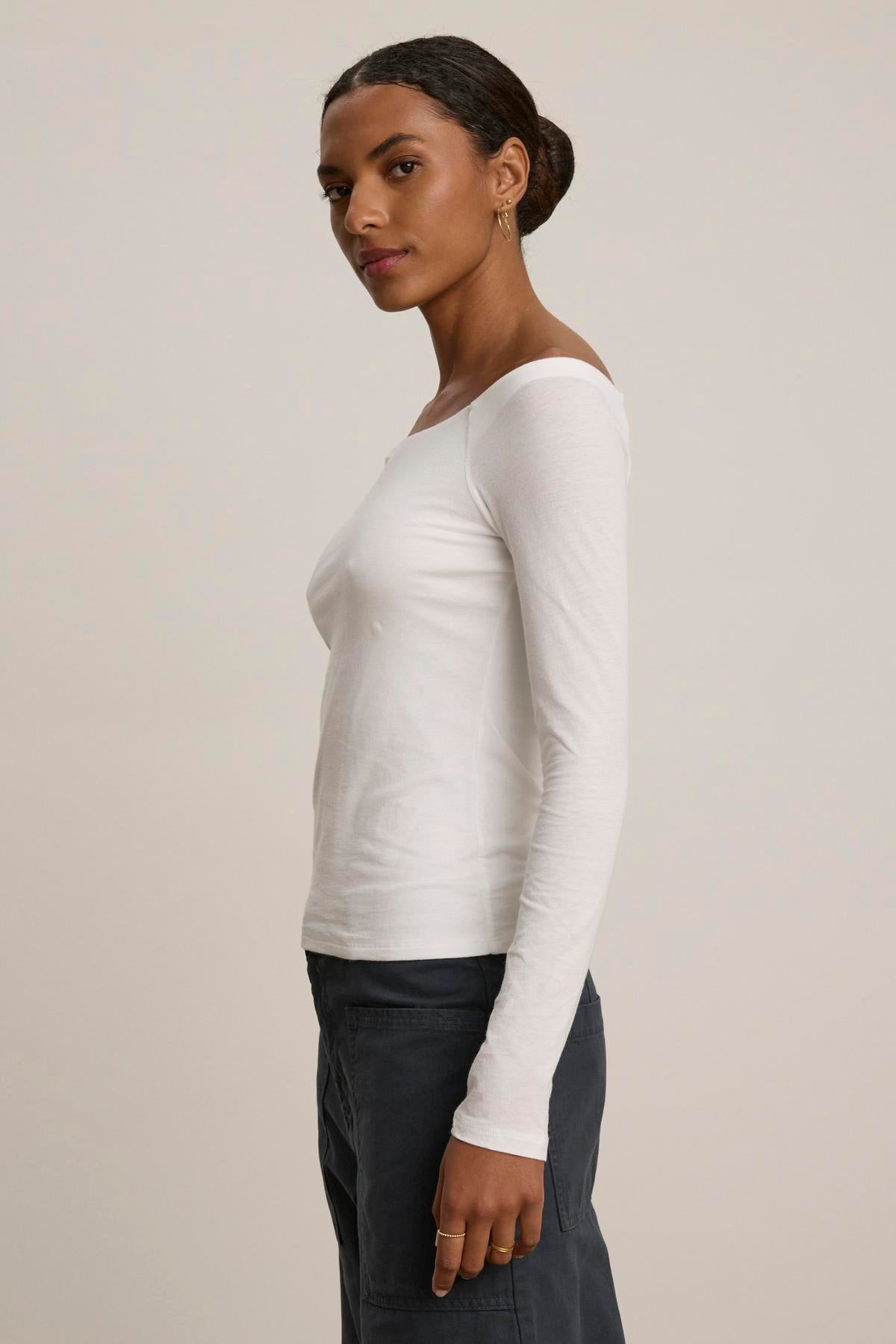 A person wearing the TANYA TEE by Velvet by Graham & Spencer, paired with dark pants, stands sideways against a plain background.-38347958485185
