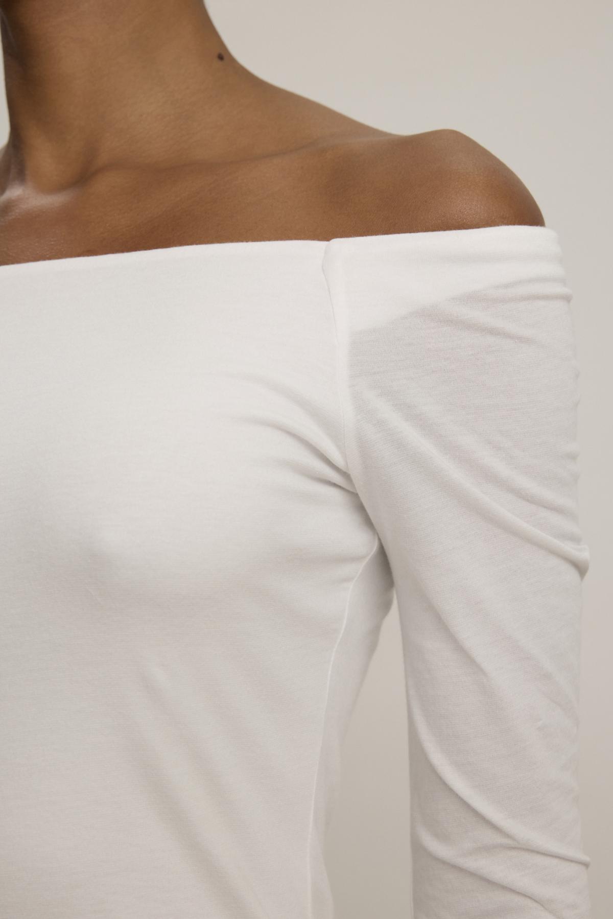 A close-up of a person wearing the TANYA TEE by Velvet by Graham & Spencer, highlighting its off-the-shoulder design and showing the neckline and part of the left arm.-38347958419649