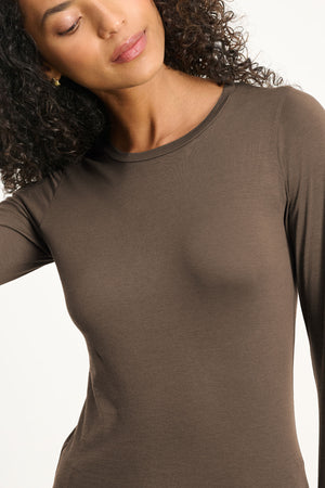 A woman with curly hair wears the ZOFINA TEE by Velvet by Graham & Spencer, a fitted long sleeve crew neck top, as she stands against a plain light background.