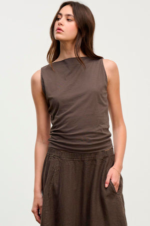 An individual dressed in the EMILIA TANK TOP by Velvet by Graham & Spencer, a soft cotton brown sleeveless tank, with a matching skirt, stands against a plain background.