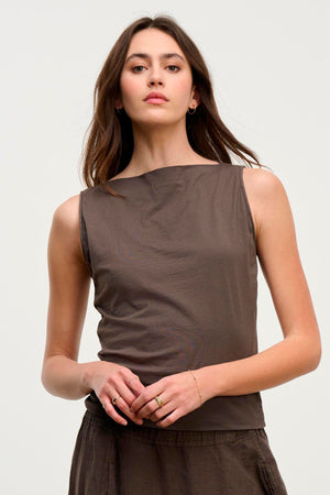 A woman with long hair wears the EMILIA TANK TOP by Velvet by Graham & Spencer. It is a sleeveless, brown top made of ultra-soft cotton fabric, against a plain background.