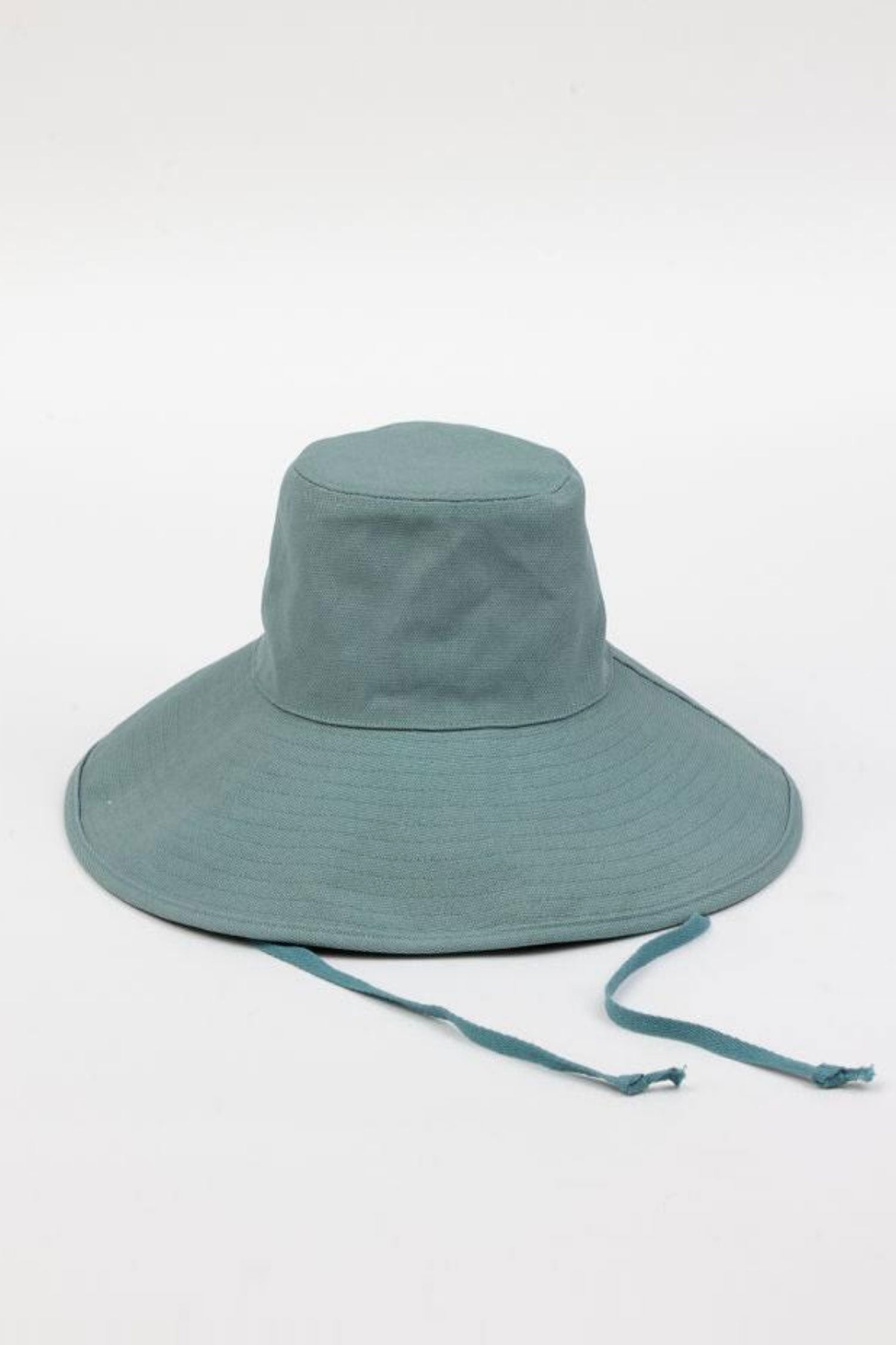 The LIVVY CANVAS SUN HAT by Velvet by Graham & Spencer is a teal wide-brimmed sun hat featuring chin straps, displayed against a plain white background.