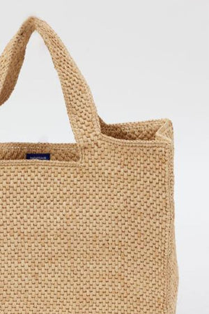 The LULU TOTE by Velvet by Graham & Spencer is a woven beige bag featuring two handles and a blue label near the top.
