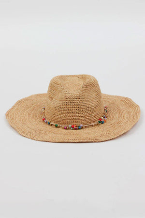 The MILL CONTINENTAL HAT by Velvet by Graham & Spencer features a wide-brimmed, woven straw design with a colorful beaded band around the crown, set against a plain background.