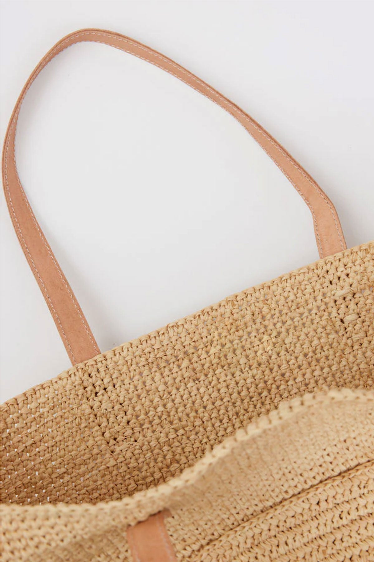A close-up shows the NAT TOTE by Velvet by Graham & Spencer, a woven beige tote bag featuring light brown leather handles, set against a white background.-38884412850369