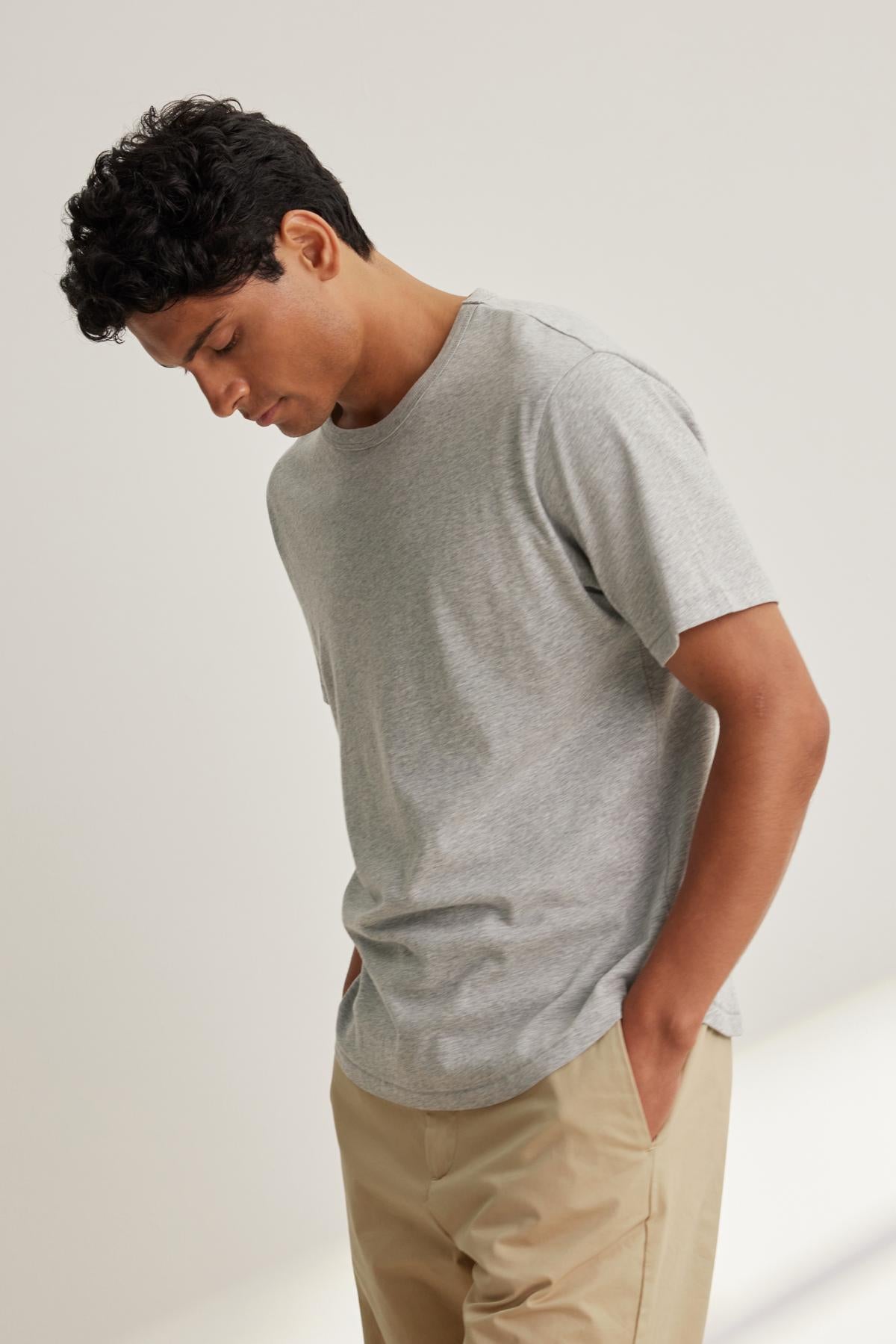 A person wearing the Velvet by Graham & Spencer MADDEN TEE in gray and beige pants stands with their head slightly tilted down.