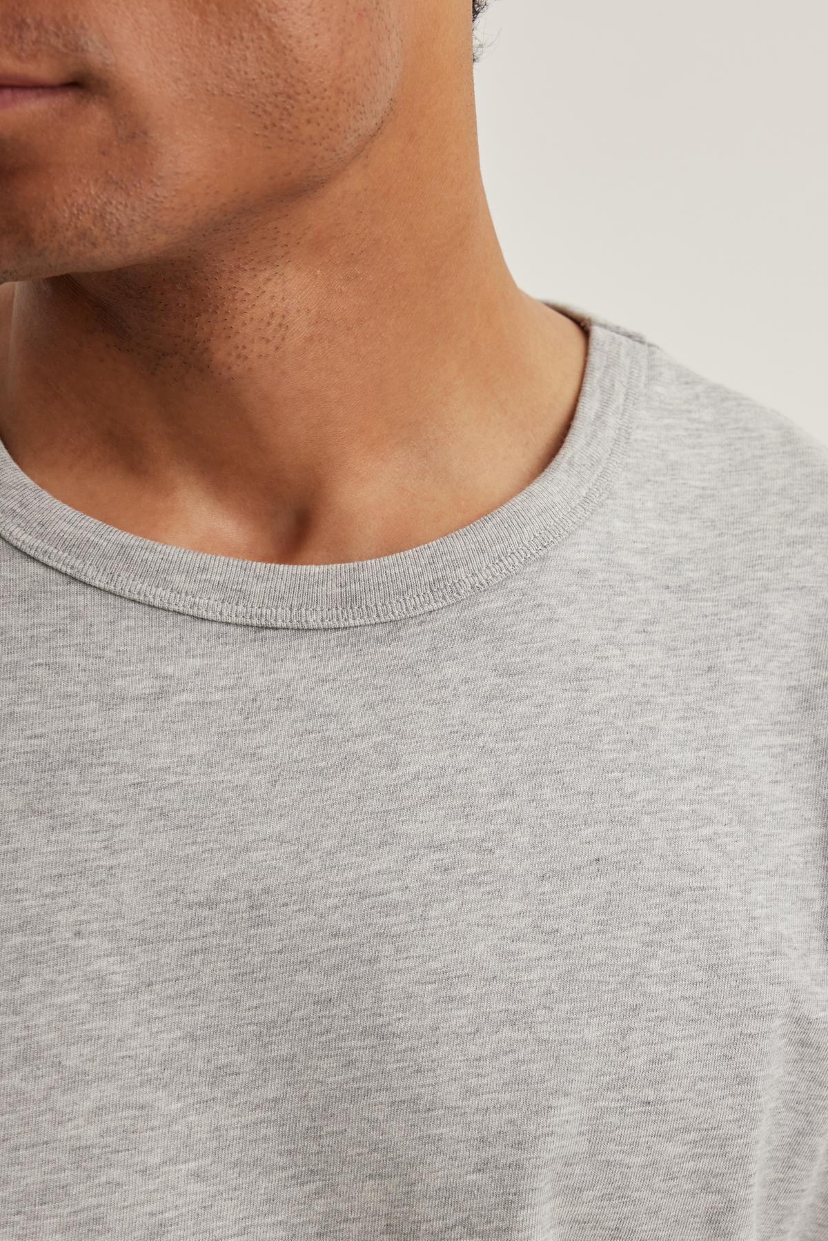 Close-up of a person wearing Velvet by Graham & Spencer's MADDEN TEE, a light gray round-neck t-shirt. Only part of the face and shoulder are visible against a neutral background.-38643316687041