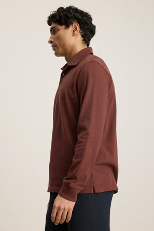 A person in profile wears the HAWKINS POLO by Velvet by Graham & Spencer, a maroon midweight jersey men's polo, paired with dark pants against a plain light background.