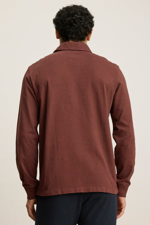 A person with short, curly black hair is seen from the back wearing the HAWKINS POLO by Velvet by Graham & Spencer, crafted from midweight jersey in a tailored fit and paired with dark pants against a plain background.