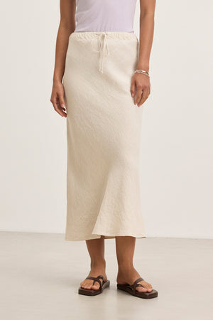 Indoors, a person dons the BEKA HEAVY LINEN SKIRT by Velvet by Graham & Spencer in beige, paired with a crisp white top.