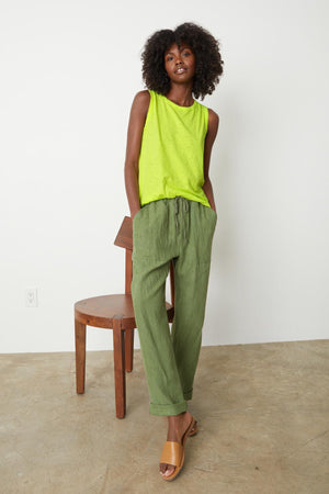 A woman standing in front of a wooden chair wearing Velvet by Graham & Spencer TAURUS COTTON SLUB TANK in bright citrus full length front with Cindy pants sandals