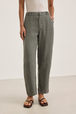 A person wearing Velvet by Graham & Spencer TAYLOR HEAVY LINEN PANT in gray-green with a white sleeveless top and brown sandals stands against a plain background, showcasing a versatile combination of style and comfort for any occasion.