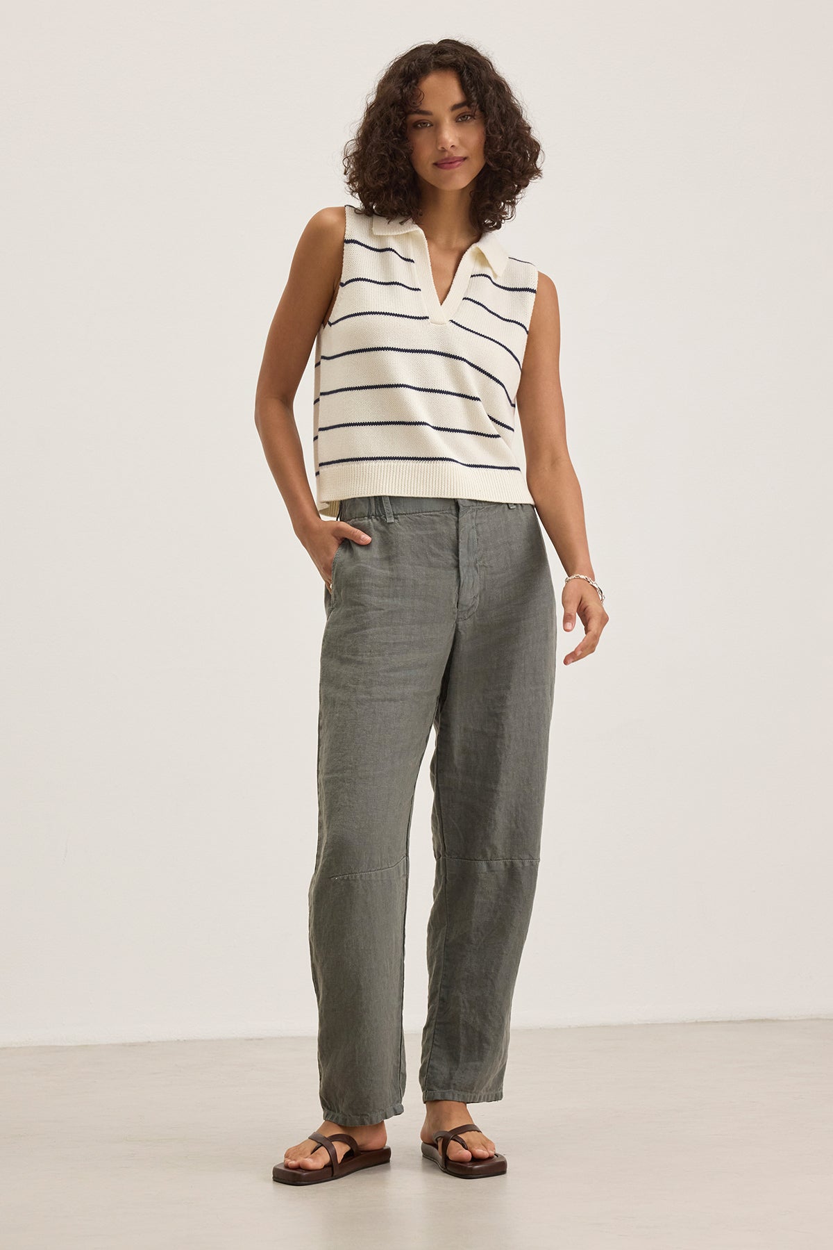 A person with curly hair wears a sleeveless striped top and the TAYLOR HEAVY LINEN PANT by Velvet by Graham & Spencer, paired with sandals, against a plain background.-38663166427329