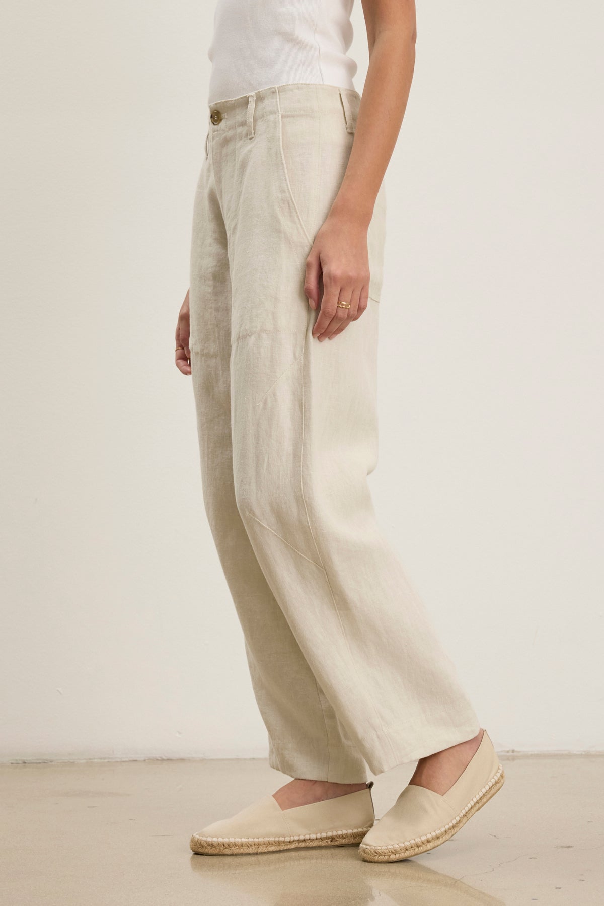 A person wears Velvet by Graham & Spencer’s ISSA HEAVY LINEN PANT in beige, styled with a white sleeveless top and beige espadrilles, standing against a plain light background.