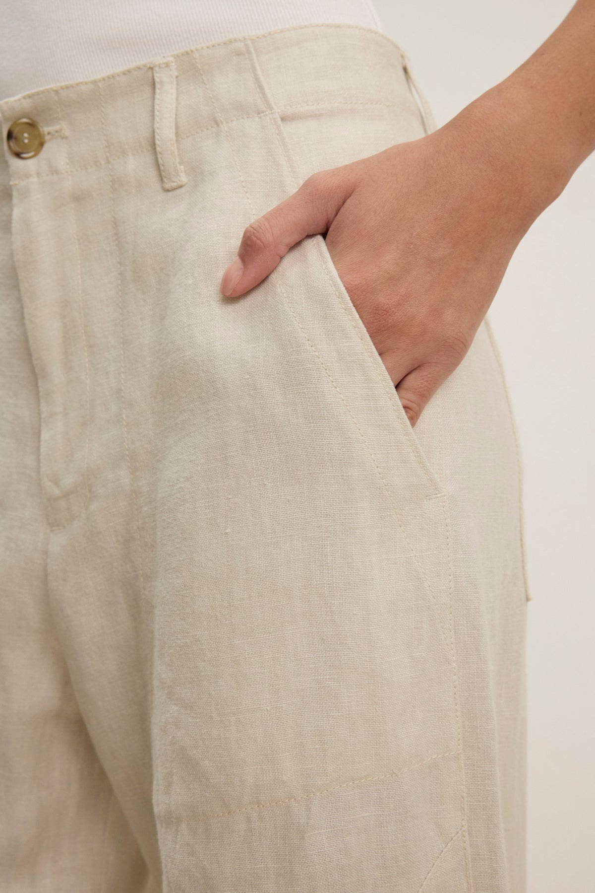 Someone wears the ISSA HEAVY LINEN PANT by Velvet by Graham & Spencer—versatile, light beige pants with a relaxed silhouette, shown from waist to mid-thigh and their right hand in the pocket.
