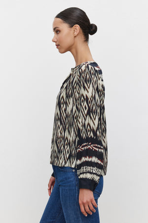 A woman in a Velvet by Graham & Spencer ABRIELLE TOP and blue jeans stands in profile against a plain background.