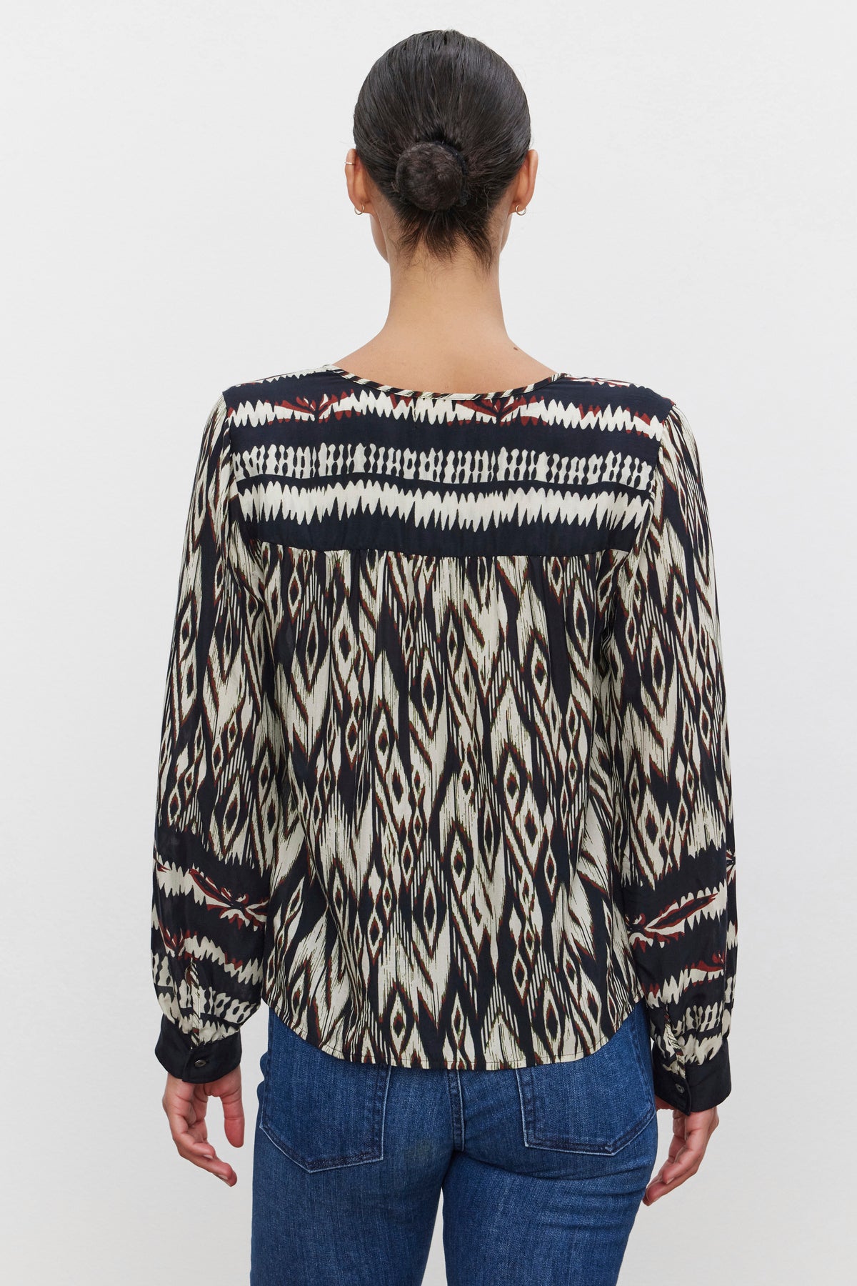 A person with dark hair tied back is wearing the ABRIELLE TOP by Velvet by Graham & Spencer and blue jeans, facing away from the camera.