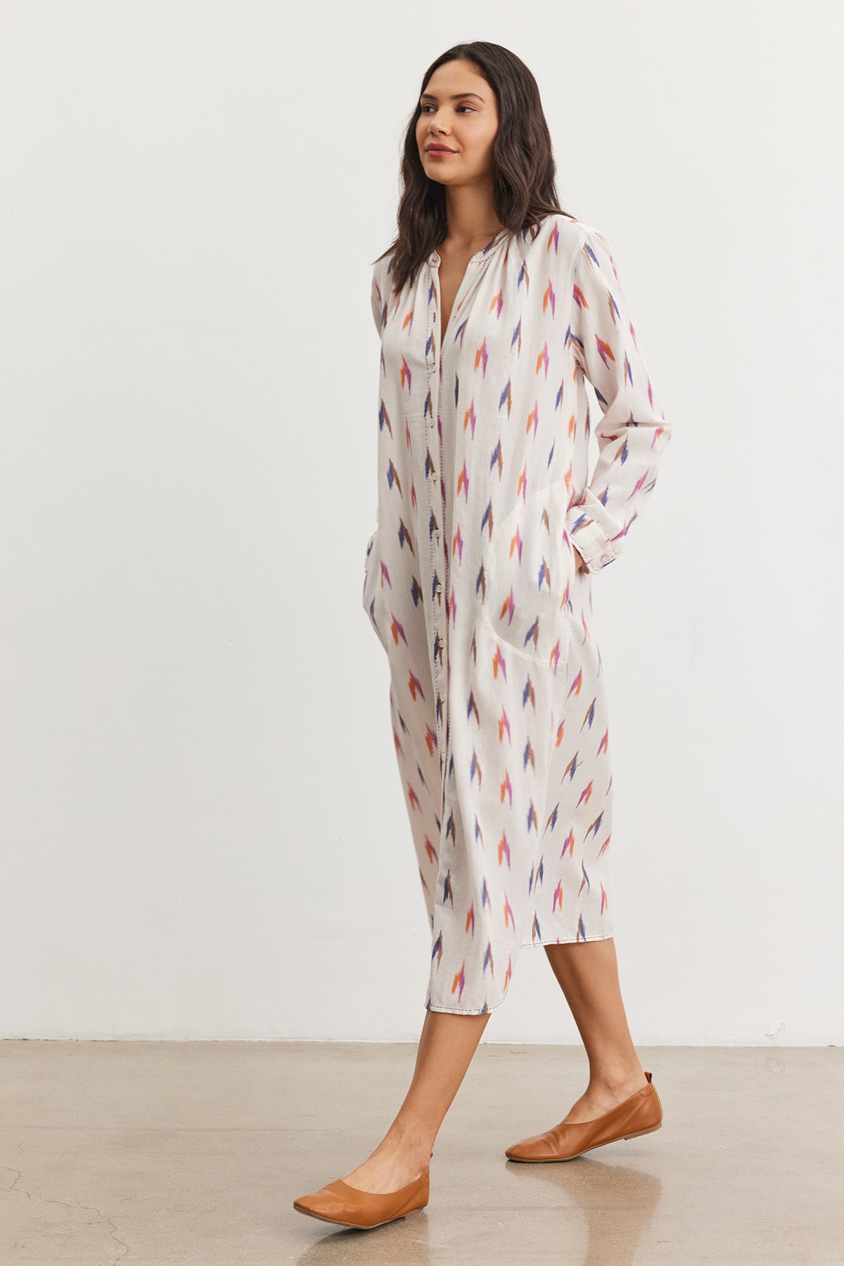 A person in the ALTA DRESS by Velvet by Graham & Spencer, featuring an ikat pattern of pointed shapes, strolls gracefully in brown flats on a plain floor.