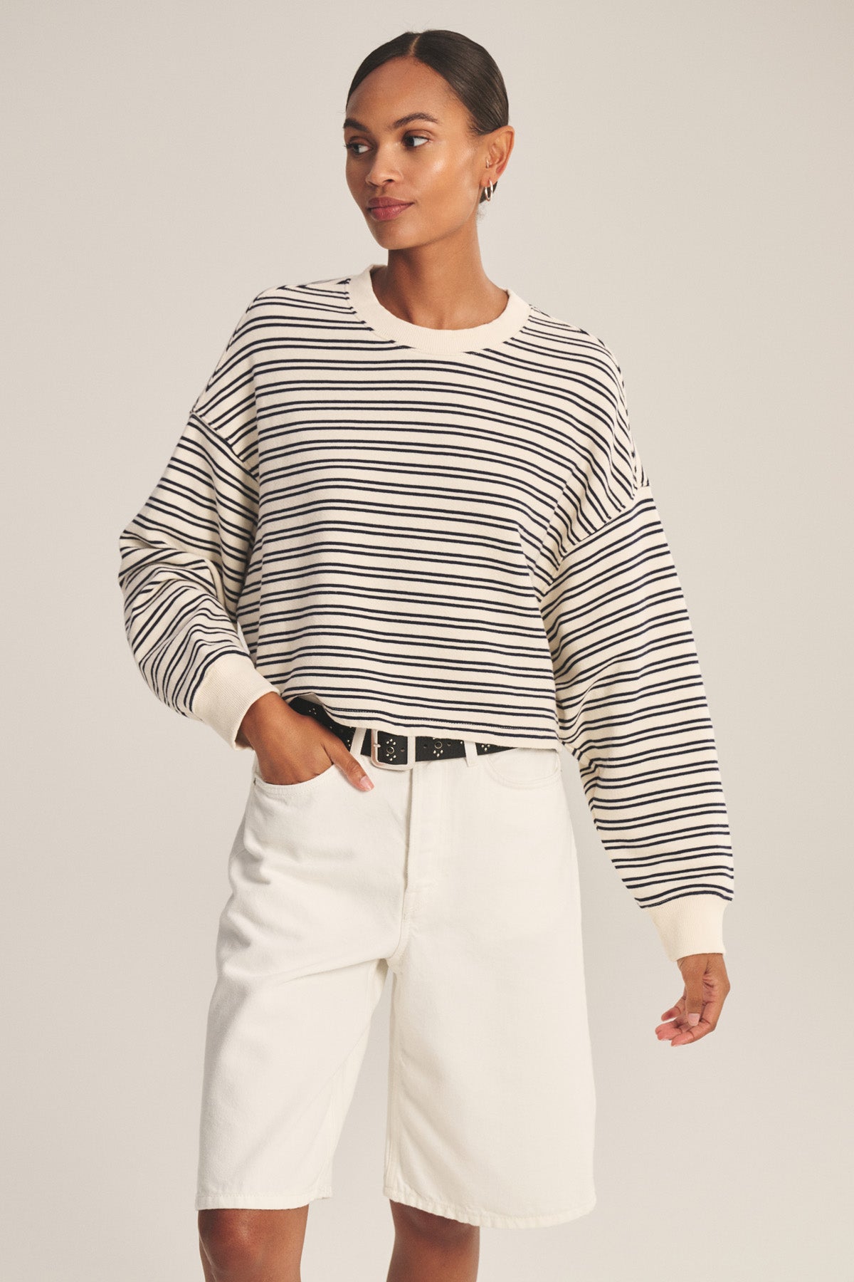 A woman models the ISABELLE PULLOVER by Velvet by Graham & Spencer—a black and white striped terry long-sleeve shirt—paired with white knee-length shorts, standing casually with one hand in her pocket against a plain background.-41088941392065