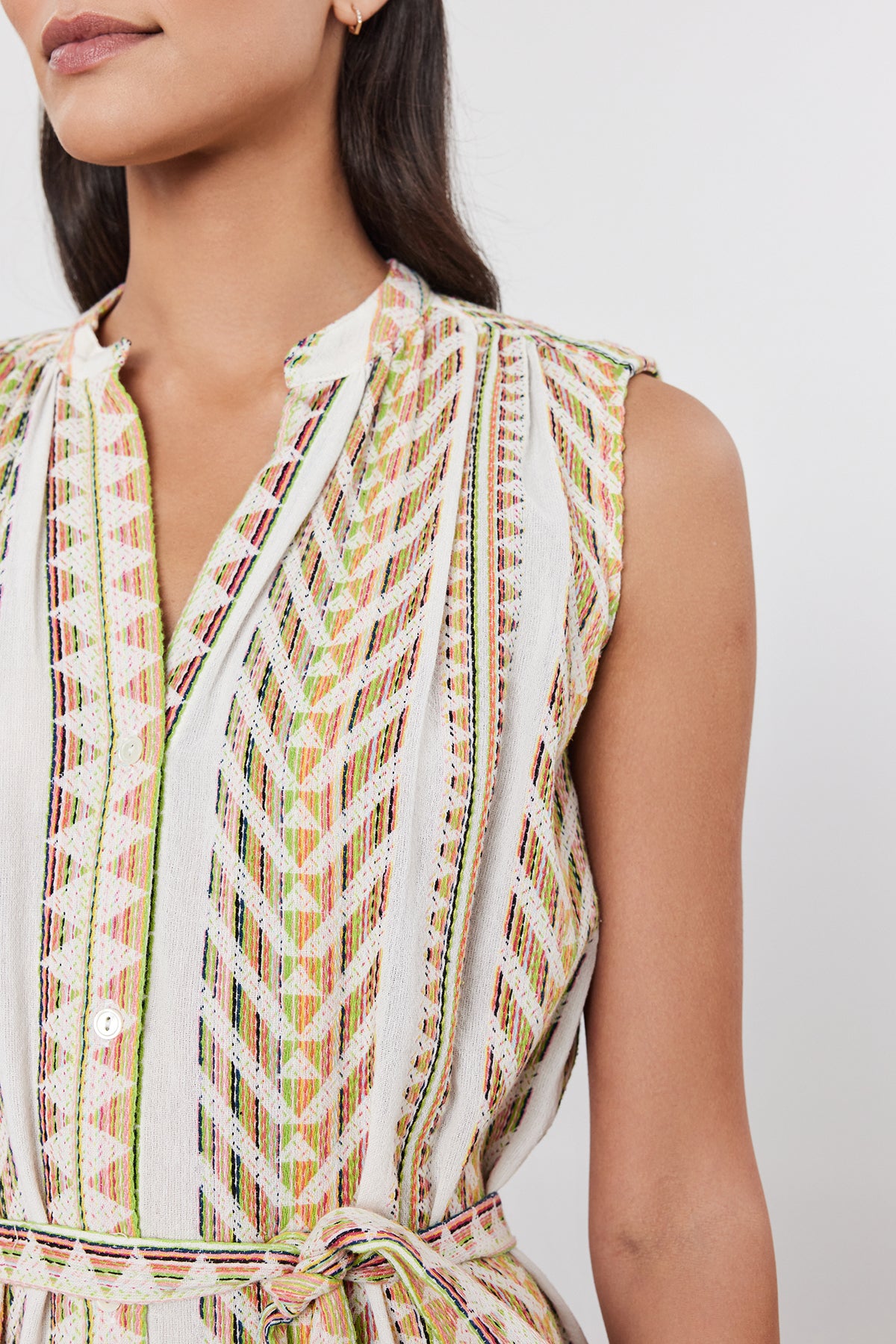 Close-up of a person wearing the ELENA DRESS by Velvet by Graham & Spencer, a sleeveless, patterned midi dress with vertical and diagonal stripes in various colors. The Jacquard striped fabric dress features a V-neck and a detachable tie belt at the waist.-37452663849153