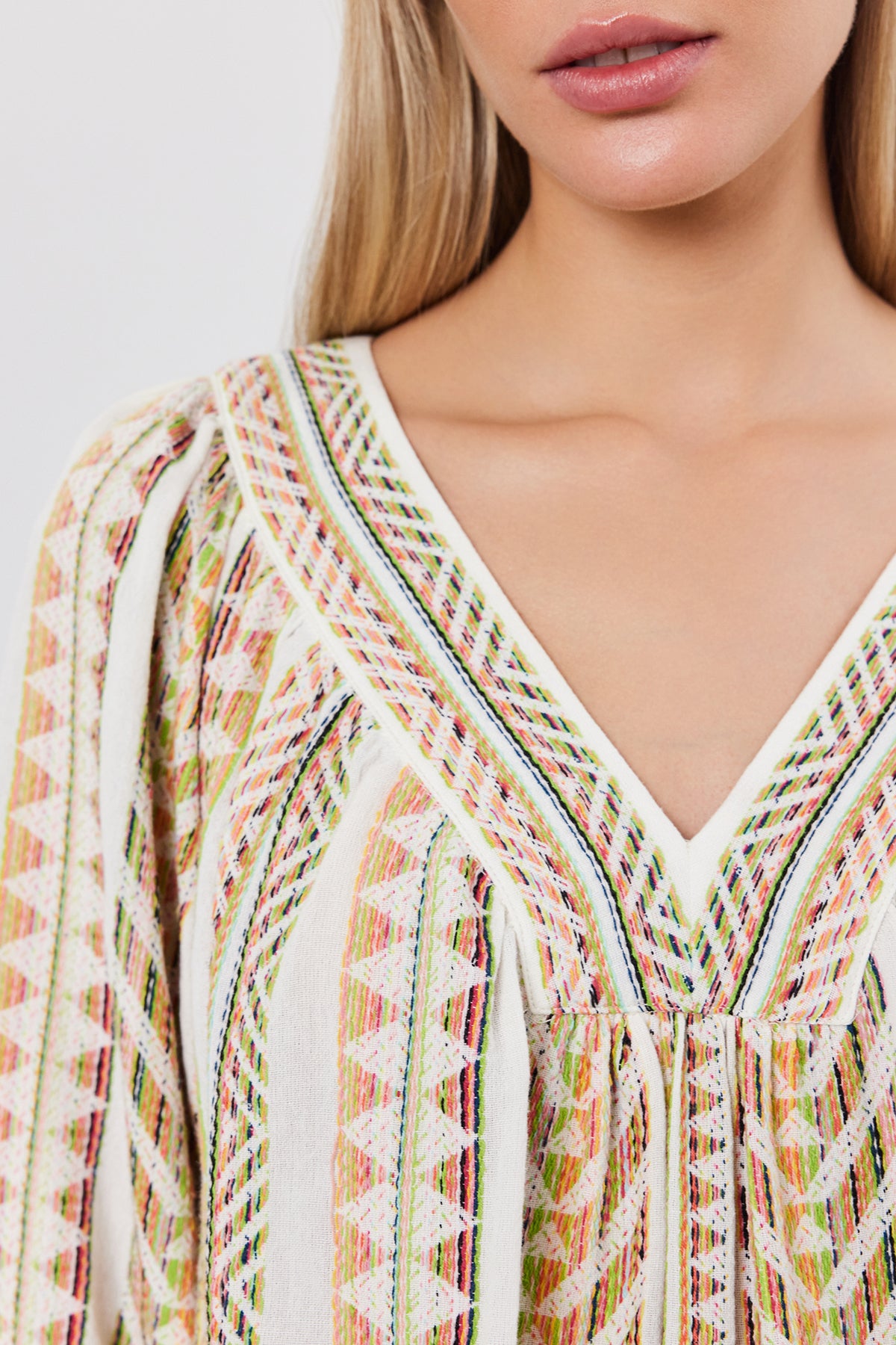 Close-up of a person's upper torso showing a colorful, patterned V-neck LILLIAN TOP with intricate embroidery and a relaxed fit by Velvet by Graham & Spencer. The image focuses on the LILLIAN TOP’s design and details, highlighting the elegant jacquard stripe pattern.-37452673024193