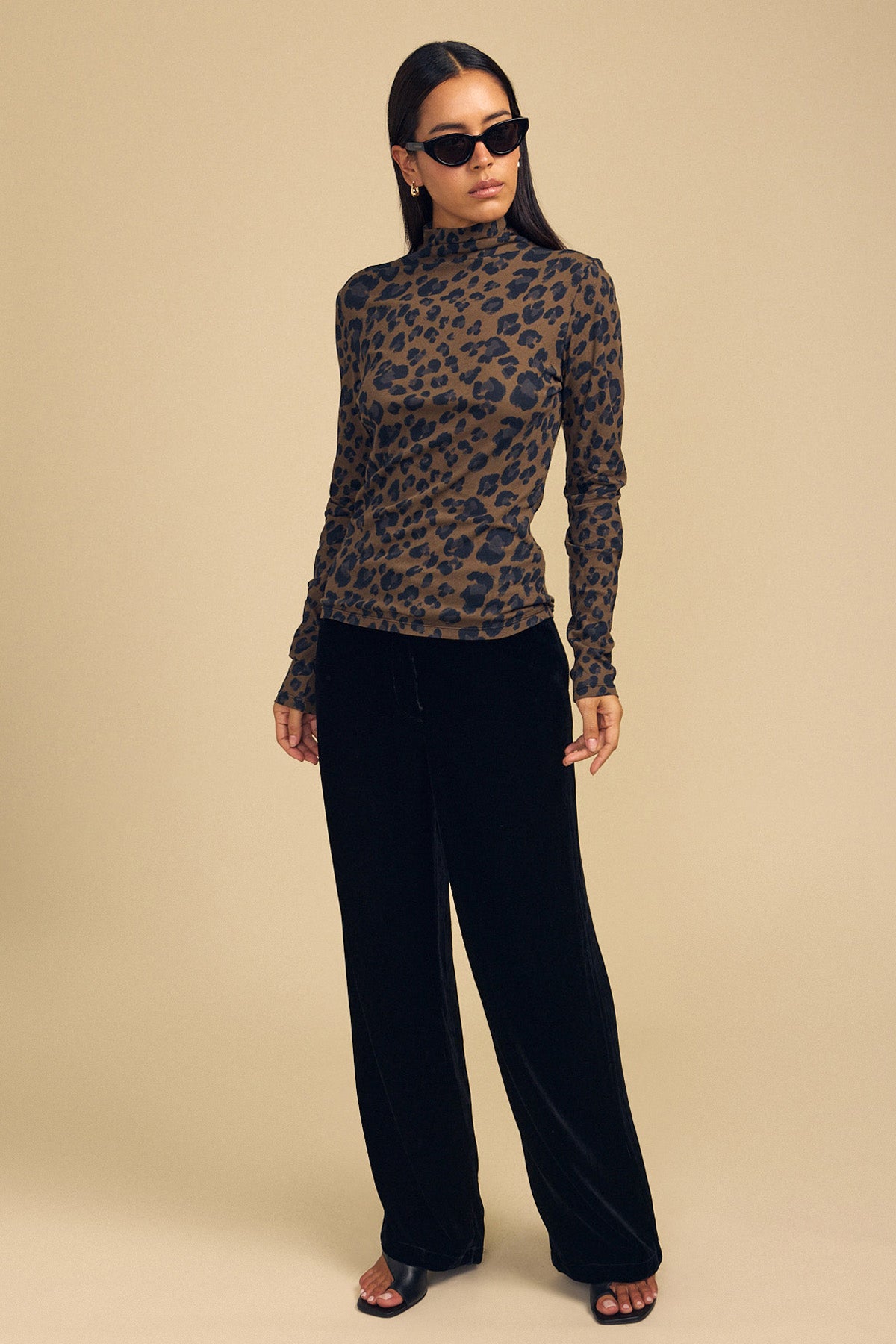 Model wearing a long-sleeved, high-neck brown leopard print ETTA TEE by Velvet by Graham & Spencer and black wide-leg trousers.-46288349135041